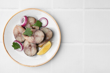 Slices of tasty salted mackerel with lemon and onion on white tiled table, top view. Space for text