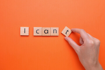 Motivation concept. Woman changing phrase from I Can't into I Can by removing wooden square with letter T on orange background, top view
