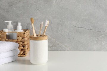 Bamboo toothbrushes in holder, towels and cosmetic products on white countertop, space for text