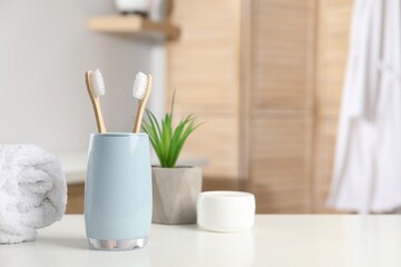 Bamboo toothbrushes, towel, potted plant and cosmetic product on white countertop in bathroom, space for text