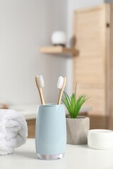 Bamboo toothbrushes, towel, potted plant and cosmetic product on white countertop in bathroom
