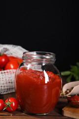 Jar of tasty tomato paste and ingredients on wooden table, space for text