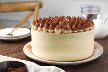 Delicious tiramisu cake with cocoa powder on wooden table, closeup