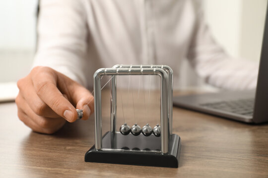 Man playing with Newton's cradle at office table, closeup. Physics law of energy conservation