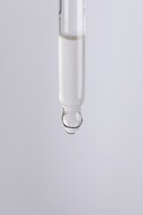 Dripping cosmetic serum from pipette on light grey background