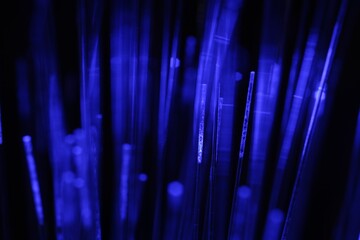 Optical fiber strands transmitting blue light on black background, macro view