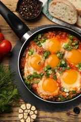 Delicious Shakshuka in frying pan served on wooden table, flat lay