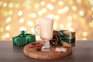 Delicious eggnog in glass and gift boxes on wooden table against blurred Christmas lights