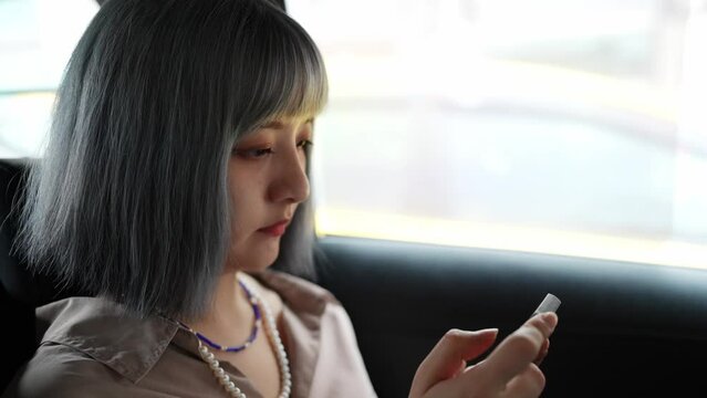 台北の都市部でタクシーに乗車してスマートフォンを操作する若い台湾人女性 A young Taiwanese woman who rides a taxi and operates a smartphone in an urban area of Taipei
