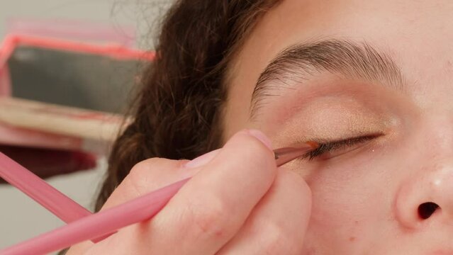 Eye shadow makeup to the upper eyelid, close-up. Makeup artist applies a bright eye shadow with a makeup brush.Tutorial master class of professional makeup. 