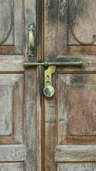 closeup of an old fashioned sliding metal handle and bolt with lock on a classic vintage wooden door 