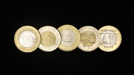 different variety of authentic ten and twenty rupee indian coins arranged in a horizontal row isolated in a black background