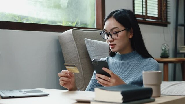 Asian woman is shopping online on her smartphone, she is placing an online order on an app and paying for the product using a credit card. Concept of online shopping and credit card payments.