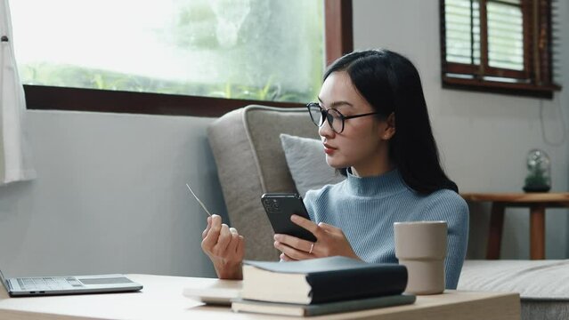 Asian woman is shopping online on her smartphone, she is placing an online order on an app and paying for the product using a credit card. Concept of online shopping and credit card payments.