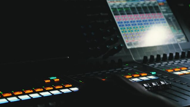 Close-up of fingers on a sound engineer's console during a concert. A professional producer controls musical parameters on a mixing console. Indicators are flashing. LED screen shows sound parameters