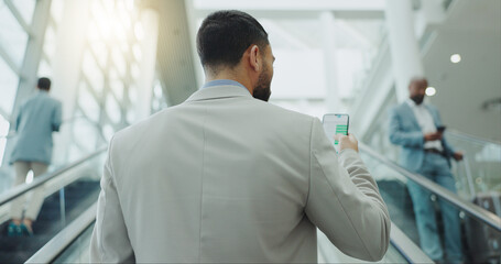 Businessman, phone and travel on escalator at airport for online booking, flight time or boarding. Rear view of man checking plane schedule on mobile smartphone for business trip on moving staircase