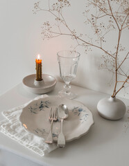 Dinner tableware serving - vintage plate, cutlery, glass, burning candle, flower arrangement on a white table