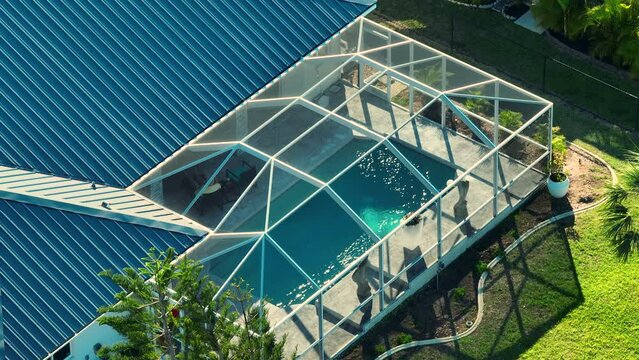 Typical contemporary American big swimming pool on backyard of private house with outside lanai enclosure covering. Concept of outdoor living and having fun in warm pool water on Florida summer sun