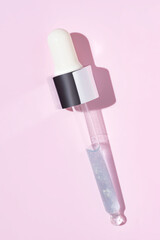 close up of pipette with pouring liquid serum and shadows on pink background. Trendy cosmetics shot with hard shadows.