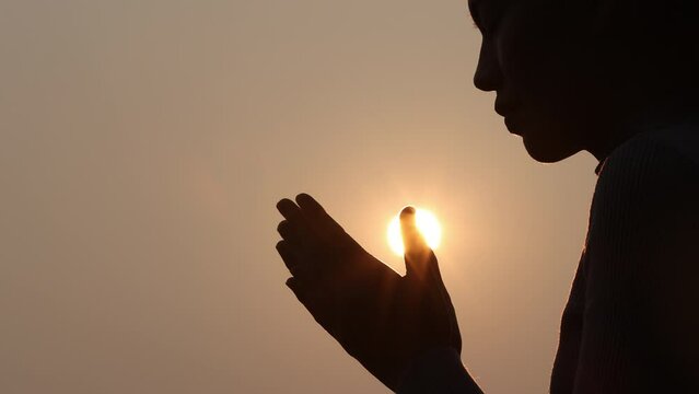 Silhouette of young human hands praying to god at sunrise, Christian Religion concept background.