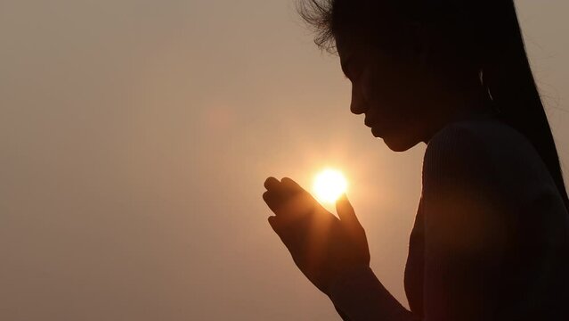 Silhouette of young human hands praying to god at sunrise, Christian Religion concept background.