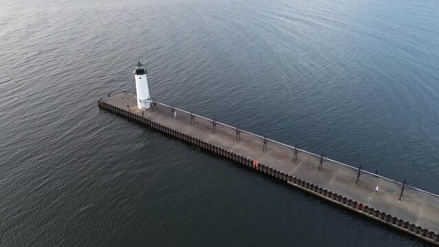 Manistee lighthouse on Lake Michigan. Very high angle aerial flyover shot of the lighthouse, pier and catwalk. Flight is over the ship channel and pans right from the lake side towards the harbor.