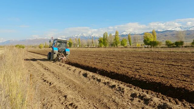 Farm Tractor Plowing a Field to Prepare for Planting.
Tractor Cultivating A Field against the background of mountains.