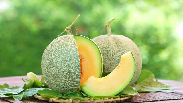 Orange Melon on blurred greenery background, Orange Melon or Cantaloupe fruit in Bamboo mat on wooden table in garden.