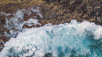 Obraz premium Atlantic ocean with strong swell beating against the walls of a rocky cliff, blue rough sea with big waves with foam crashing against the rocks, south of Tenerife, Canary island