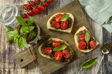 Homemade bruschetta with pesto sauce, fresh tomatoes on a wood background. Traditional italian appetizer or snack, antipasto. View from above.