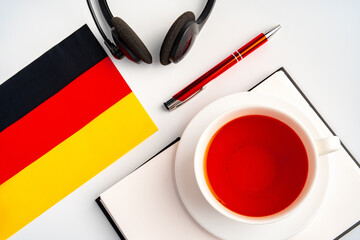 Notepad with German flag and headphones on white background. German language audio courses...