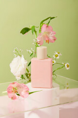 The front of the pastel pink unbranded perfume bottle is placed on a white podium with different types of flowers. Creative space for cosmetic advertising.