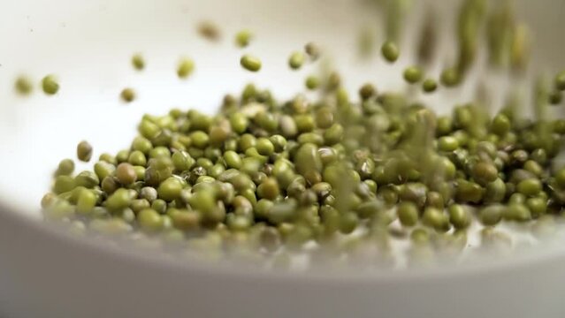 Raw green mung beans falling into a bowl in slow motion close up. Food dietary ingredient