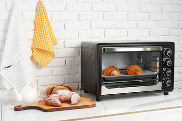 Modern mini electric oven with freshly baked croissants in kitchen