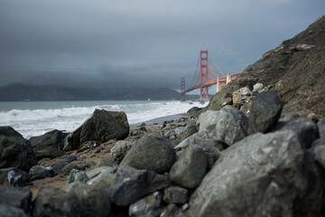 In the foreground, large rocks are strewn across a beach, taking up much of the frame. In the...