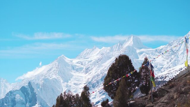 4K shot of snow covered Himalayan mountain peak with prayer flags waving in the wind in front of it as seen from Shashur Monastery in Keylong, Himachal Pradesh, India. Snowy mountain in winter Lahaul.