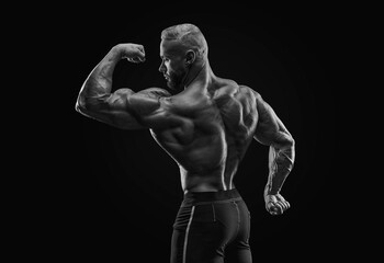 Silhouette of a strong bodybuilder. View from the back. Confident young fitness athlete with a powerful body and perfect abs. Black and white photography.
