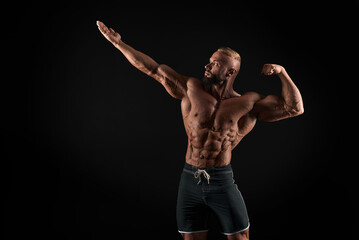 Fototapeta na wymiar Muscular man shows his muscles against the background of a black wall. Bodybuilder, male naked torso, abs.