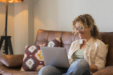 One relaxed happy woman smile and using laptop computer sitting comfortably on the sofa at home. Female people chatting and dating online. Modern lady surfing the net and chat with friends remote