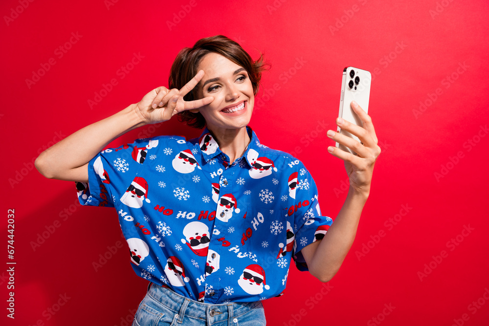 Canvas Prints Portrait of attractive friendly person hold smart phone make selfie show v-sign near eye isolated on red color background