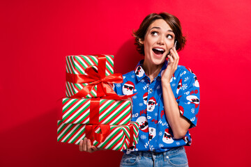 Photo of joyful young lady gifts for christmas noel party wrapped boxes dialogue phone call look curious isolated on red color background