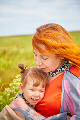 Happy female family with mother and daughter on green and yellow meadow full of grass and flower. Woman with red hair and blonde girl having fun, joy and hugs in sunny summer day. Concept family love
