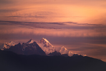 Mount kangchenjunga peak of Himalayan mountains during sunrise. Snow clad golden white peaks under cloud cover as seen fro kalimpong india.