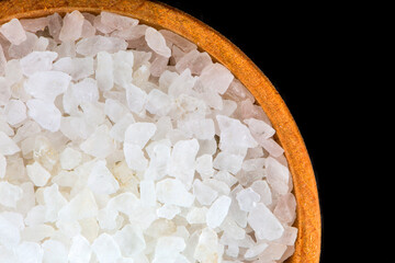 White bath salt in a wooden bowl closeup isolated on black background