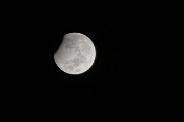Partial lunar eclipse where full moon is under shadow of earth. Photo of astronomical event taken against dark night sky.