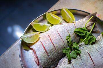 Raw fish kept on a plate, nicely cleaned and scored, marinated with lemon wedges and coriander leaves for cooking. Eating fish has many health benefits