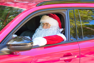 Santa Claus in glasses and white gloves sits in a red car and looks ahead. Close-up portrait
