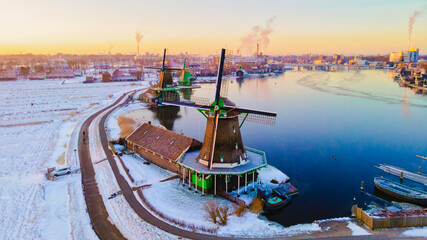 Zaanse Schans Netherlands a Dutch windmill village during sunrise at winter with a snowy landscape, winter snow at the historical windmill village near Amsterdam during sunrise - obrazy, fototapety, plakaty