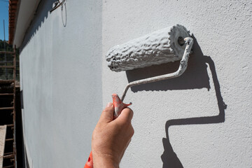 Mão de pintor a segurar um rolo cheio de tinta para pintar uma parede exterior