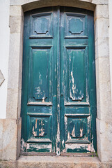 Old traditional wooden door with wrought iron door knockers on white facade in Portugal